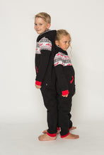 Load image into Gallery viewer, Sofa Killer black unisex kids onesie Nordic on two kids standing back to back, highlighting the fun holiday design with red accents and cozy fit.