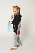 Load image into Gallery viewer, Side view of a child wearing the Sofa Killer tricolor unisex kids onesie Racing, highlighting the red pocket and colorful design with cheer accessories.