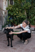 Load image into Gallery viewer, Woman wearing the Paloma linen black jumpsuit, kneeling down to pet a black dog surrounded by greenery.