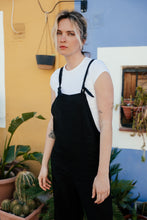 Load image into Gallery viewer, Woman in the Paloma linen black jumpsuit with adjustable straps, posing in front of a colorful wall, exuding a casual yet stylish vibe.