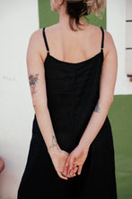 Load image into Gallery viewer, Back view of a woman wearing the Women's Black Linen Jumpsuit Vega, highlighting the adjustable straps and minimalist design with tattoos visible on her arms.