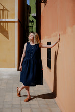 Load image into Gallery viewer, Model showcasing the Women's dark blue linen sleeveless dress Costa Blanca by SofaKiller, standing against a warm-toned wall in a sunny street.
