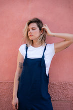 Load image into Gallery viewer, Close-up of the model in a Linen dark blue color jumpsuit with adjustable straps Paloma, highlighting the effortless style and casual vibe against a textured pink backdrop.