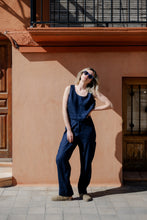 Load image into Gallery viewer, Model wearing Sofa Killer dark blue linen trousers Lucia, posing against a rustic wall with sunglasses and a casual look.