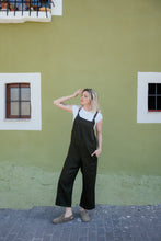 Load image into Gallery viewer, Model wearing a linen dark brown color jumpsuit with adjustable straps from Sofa Killer, styled casually against a vibrant green wall.