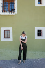 Load image into Gallery viewer, Woman wearing a linen dark brown color jumpsuit with adjustable straps Paloma, standing against a green wall.