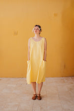 Load image into Gallery viewer, A model wearing Women's yellow linen sleeveless dress Marisol by SofaKiller, featuring deep side pockets, against a vibrant yellow wall, perfect for summer outings.