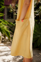 Load image into Gallery viewer, Detail shot of the side of the Women's yellow linen sleeveless dress Marisol by SofaKiller, emphasizing the functional pocket and the dress's light fabric in a sunny outdoor setting.