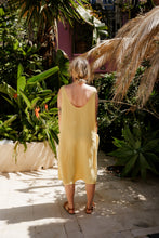 Load image into Gallery viewer, Back view of a woman in the Women's yellow linen sleeveless dress Marisol by SofaKiller, featuring a low back design, as she stands in a scenic garden filled with tropical plants.