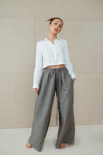 Load image into Gallery viewer, Front view of a woman confidently posing in Sofa Killer natural green linen trousers, revealing pockets and luxurious fabric.