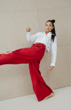 Load image into Gallery viewer, Dynamic pose of a model in Sofa Killer red linen trousers Doha and a white crop shirt, illustrating the flowy design and stylish vibe.