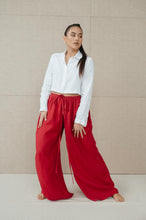 Load image into Gallery viewer, Model in Sofa Killer red linen trousers Doha striking a fashionable pose with a white crop shirt, showcasing its chic appeal.