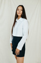 Load image into Gallery viewer, Natural white linen crop top JARAN styled with a high-waisted shorts, model showcasing the long sleeves and collared design.