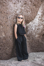 Load image into Gallery viewer, Sofa Killer linen black girl set with a young girl leaning against a rock, showcasing her black linen outfit and trendy sunglasses.