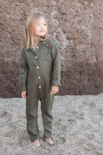 Load image into Gallery viewer, Child wearing a Sofa Killer linen dark green color unisex kids onesie, standing on sandy ground with a cheerful expression.