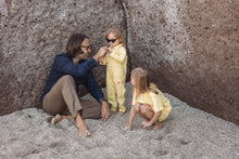 Load image into Gallery viewer, A father interacting with two children in Sofa Killer yellow color unisex kids onesies, enjoying playtime in a sandy environment.