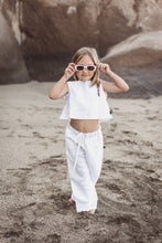 Load image into Gallery viewer, Sofa Killer linen white girl set featuring a young girl wearing stylish white linen top and trousers, posing on a sandy beach with sunglasses.