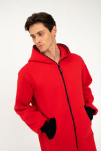 Load image into Gallery viewer, Close-up of the Sofa Killer red onesie Texas with black zipper, showcasing the hood and pockets on the model.