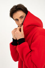 Load image into Gallery viewer, Model adjusting the hood of the Sofa Killer red onesie Texas with black zipper, emphasizing the comfy design.