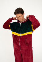 Load image into Gallery viewer, Sofa Killer California velour onesie in bordo, green, and yellow, worn by a man adjusting the hood, showcasing the cozy and stylish design perfect for lazy days or festivals.