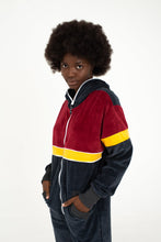 Load image into Gallery viewer, Sofa Killer women velour onesie Kansas worn by a model with an afro hairstyle, featuring a maroon, yellow, and dark grey color combination.