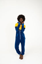 Load image into Gallery viewer, Sofa Killer women velour onesie Dakota in royal blue and yellow, featuring a hood and zip closure, modeled by a woman with natural hair, perfect for cozy days.