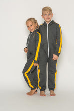 Load image into Gallery viewer, Sofa Killer dark grey unisex kids onesie with yellow vertical lines, featuring two children standing together, smiling and wearing the comfy onesie.
