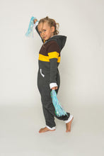 Load image into Gallery viewer, Sofa Killer tricolor unisex kids onesie GYL, depicting a playful child in a dark grey onesie with yellow and brown accents, striking a fun pose while holding colorful pom-poms.

