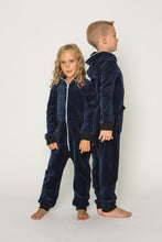 Load image into Gallery viewer, A child wearing a Sofa Killer dark blue unisex kids velours onesie, posing sideways, showing off the outfit details.
