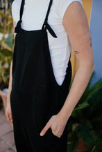 Load image into Gallery viewer, Close-up view of a woman wearing the 'Linen black color jumpsuit with adjustable straps Paloma', showcasing the loose fit and pockets.
