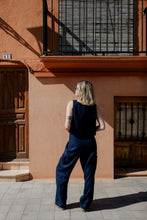 Load image into Gallery viewer, Back view of a model showcasing Sofa Killer dark blue linen trousers Lucia, highlighting the relaxed fit and casual vibe in an outdoor setting.
