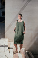 Load image into Gallery viewer, Women's Dark Green Linen Sleeveless Dress Lola by SofaKiller, showcasing a model standing stylishly in a relaxed, knee-length fit with side pockets against a sunlit wall.
