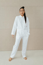Load image into Gallery viewer, Sofa Killer white linen women onesie showcased on a model standing confidently against a light backdrop. The onesie features a relaxed fit, long sleeves, and a waist-adjusting belt, perfect for summer outings.
