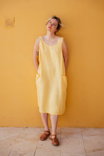 Load image into Gallery viewer, Women's yellow linen sleeveless dress Marisol by SofaKiller, styled on a model against a matching yellow wall, showcasing a relaxed fit and deep side pockets.
