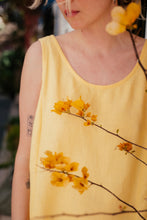 Load image into Gallery viewer, Detail shot of the Women's yellow linen sleeveless dress Marisol by SofaKiller, featuring a model holding yellow flowers, highlighting the dress's vibrant color.
