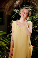 Load image into Gallery viewer, Casual pose of a model in the Women's yellow linen sleeveless dress Marisol by SofaKiller, enjoying the sun in a vibrant garden, showcasing comfort and style.
