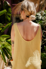 Load image into Gallery viewer, Close-up of a woman wearing the Women's yellow linen sleeveless dress Marisol by SofaKiller, highlighting the stylish low back design, complemented by beautiful garden scenery.
