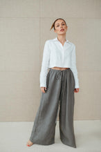 Load image into Gallery viewer, Casual pose of a woman in Sofa Killer natural green linen trousers, showcasing comfort and style with a cropped white shirt.
