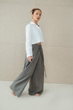 Load image into Gallery viewer, Side view of a woman modeling Sofa Killer natural green linen trousers, highlighting the drawstring detail and wide leg silhouette.

