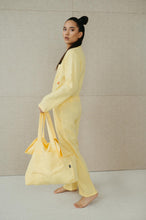 Load image into Gallery viewer, Model walking away gracefully with a tote bag, dressed in a Sofa Killer lime yellow linen women onesie, perfect for casual outings.
