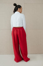 Load image into Gallery viewer, Back view of Sofa Killer red linen trousers Doha styled with a white crop shirt, highlighting the comfortable wide fit.
