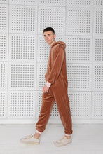 Load image into Gallery viewer, Sofa Killer brown velours men's onesie showcased on a model standing against a textured white wall, perfect for casual summer outings and comfortable wear.
