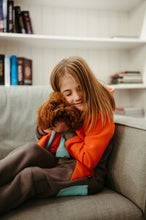 Load image into Gallery viewer, Girl embracing her small dog, both in matching dog onesie style Jordan, showcasing love and comfort on the sofa.
