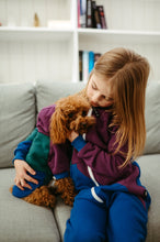 Load image into Gallery viewer, Sofa Killer tricolor unisex kids onesie Groove, with a child cuddling a puppy on a sofa, showcasing the colorful design with dark green sleeve, violet top, and dark blue bottom.
