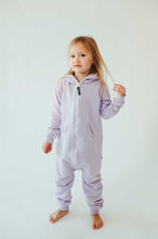 Load image into Gallery viewer, Sofa Killer unisex kids onesie Medusa in light purple, featuring a white zipper, worn by a young girl standing with bare feet and one hand playing with her hair.
