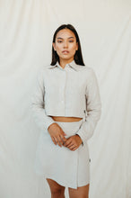 Load image into Gallery viewer, Natural white linen crop top JARAN featuring buttons, a collar, and long sleeves, modeled by a woman standing against a neutral backdrop.
