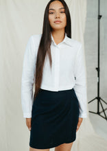 Load image into Gallery viewer, Natural white linen crop top JARAN featured on a model, displaying the buttoned front and long sleeves paired with a chic skirt.
