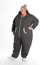 Load image into Gallery viewer, Sofa Killer dark grey plus size adult onesie with light grey cuff, modeled by a curvy woman in a standing pose. The cozy onesie features a zippered front and side pockets, perfect for comfort and warmth.
