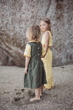 Load image into Gallery viewer, Two girls enjoying a day at the beach. One girl is wearing a Sofa Killer dark green dress with yellow details, showcasing a stylish back button closure, while the other girl sports a light yellow outfit. Perfect for capturing special moments!
