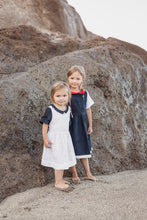 Load image into Gallery viewer, Two girls in Sofa Killer linen white dress with blue color details, captured alongside a rocky backdrop, emphasizing the dress's comfort and style for family gatherings.
